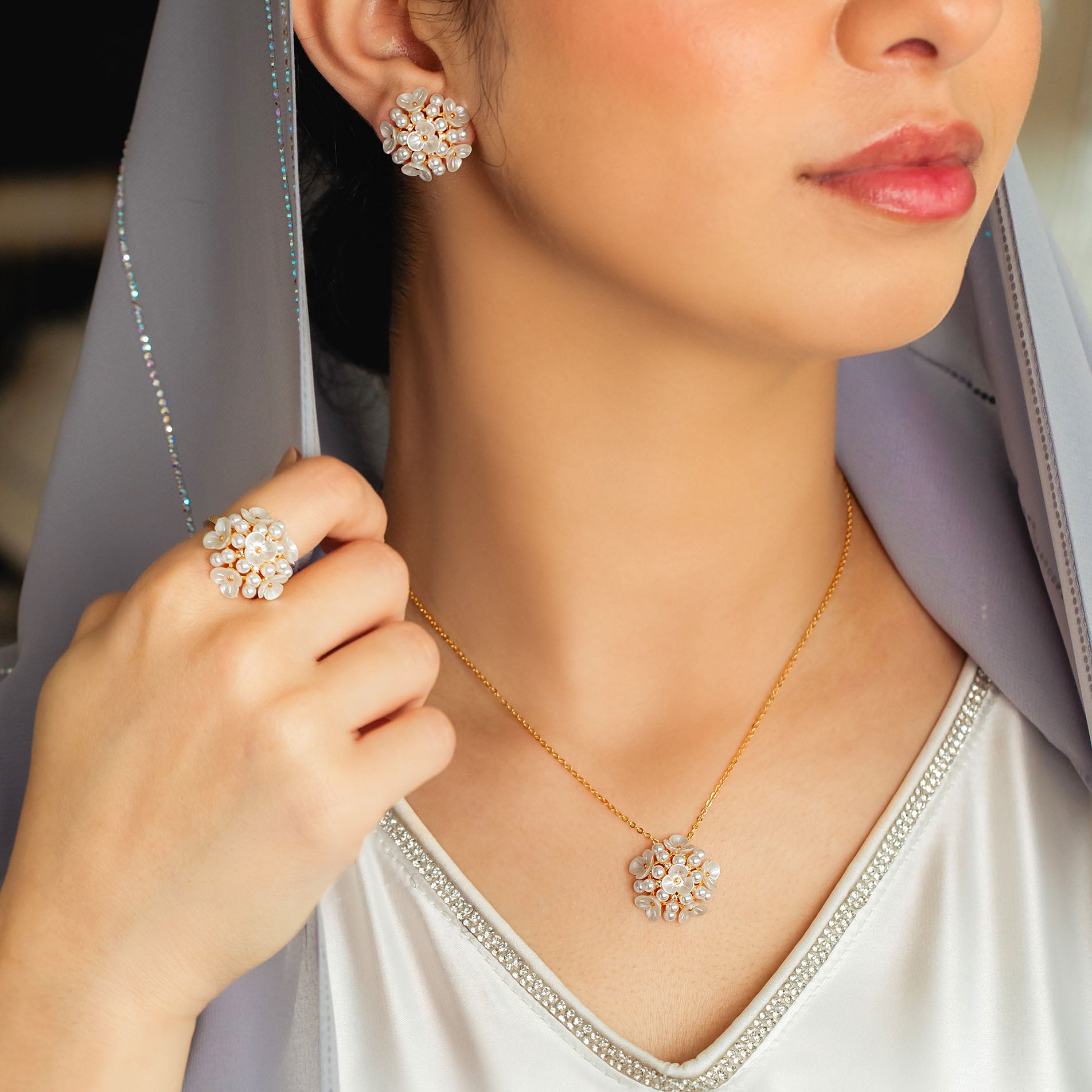 A person wearing a gold-plated faux pearl necklace and earrings set with intricate designs.