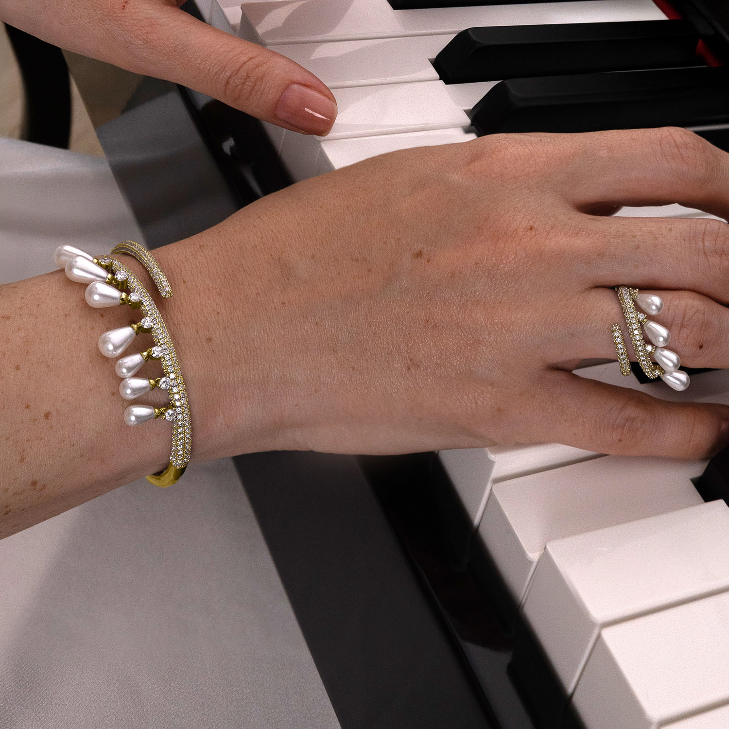 Hand with pearl bracelet and rings on a piano keyboard