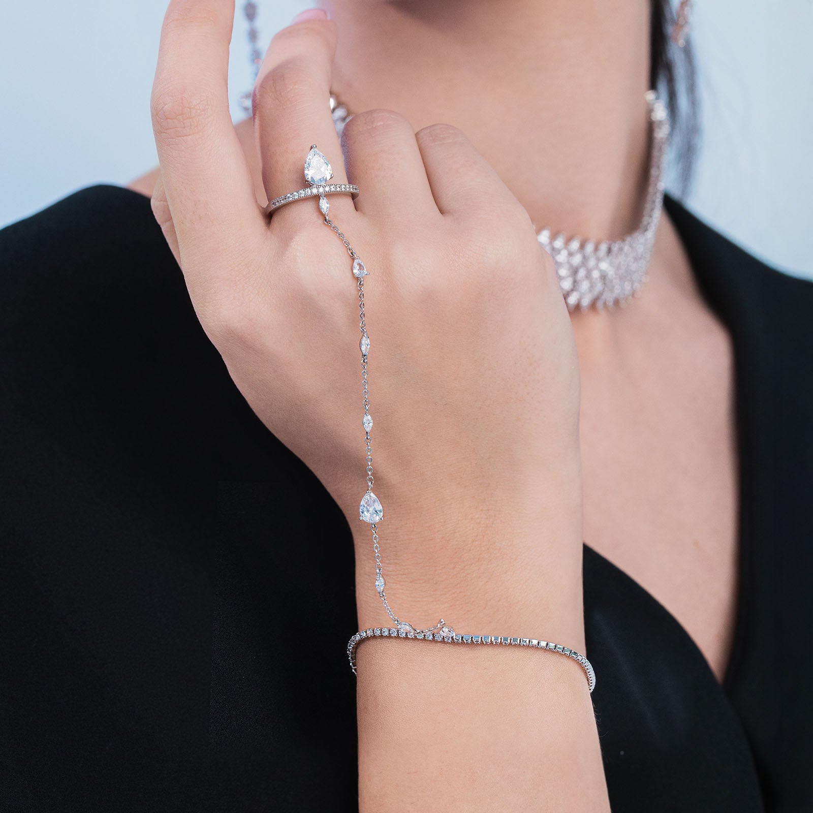 Close-up of a hand wearing multiple diamond jewelry pieces including a bracelet, ring, and necklace.