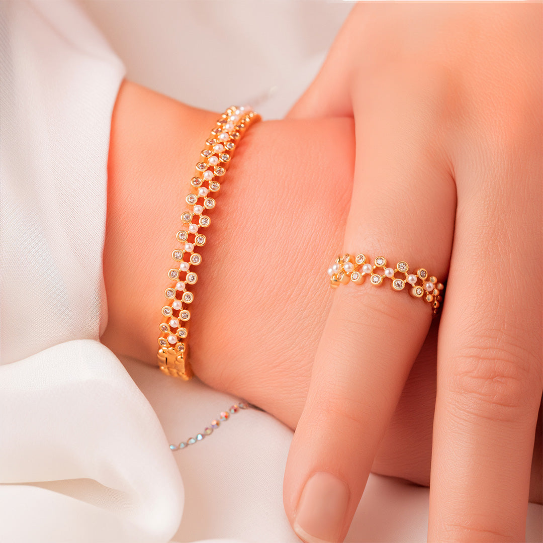 A set of gold-plated bangle bracelets with pearl embellishments, displayed on a person's wrist.
