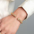 Gold bracelets on a person's wrist against a neutral background
