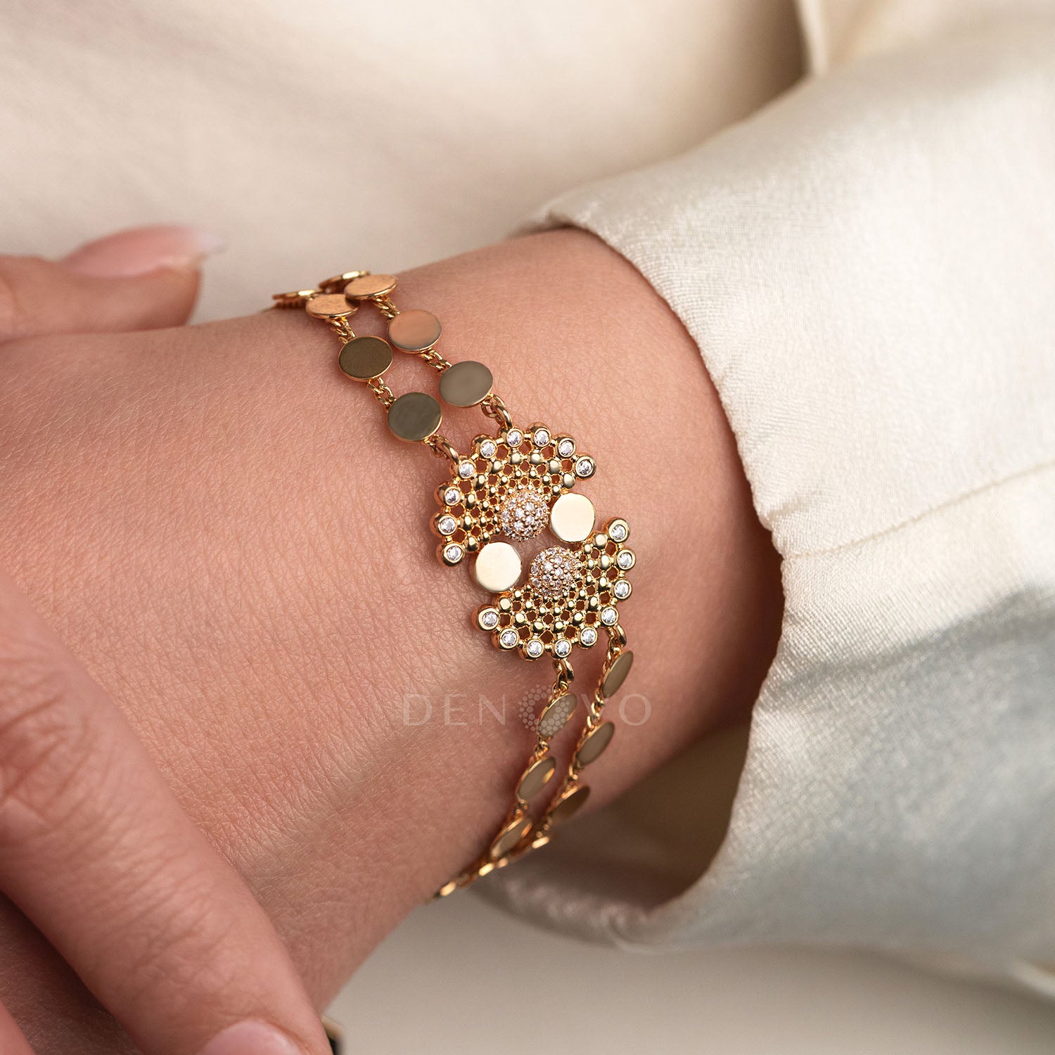 Gold bracelet with circular design on a wrist against a neutral background