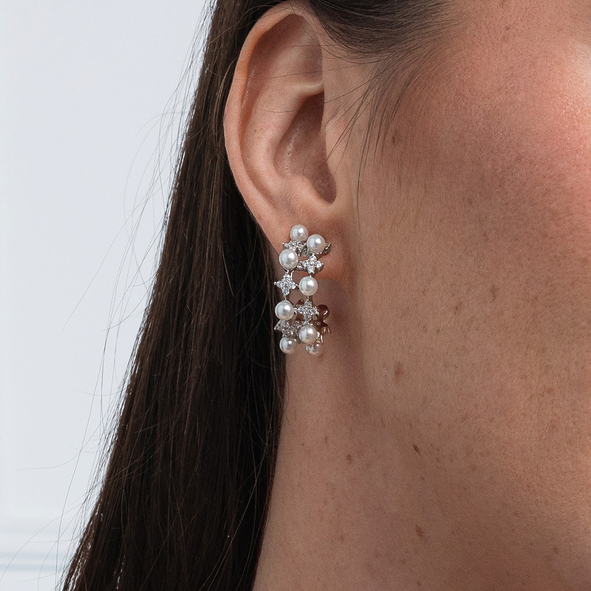 Close-up of an ear wearing a pearl earring with a white background