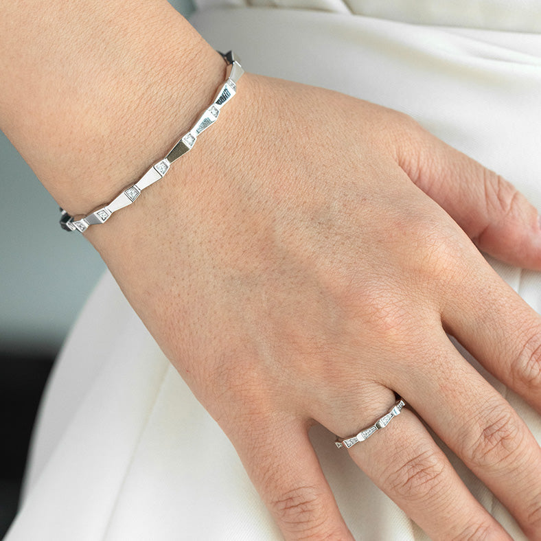 Hand wearing a silver bracelet and ring on a neutral background