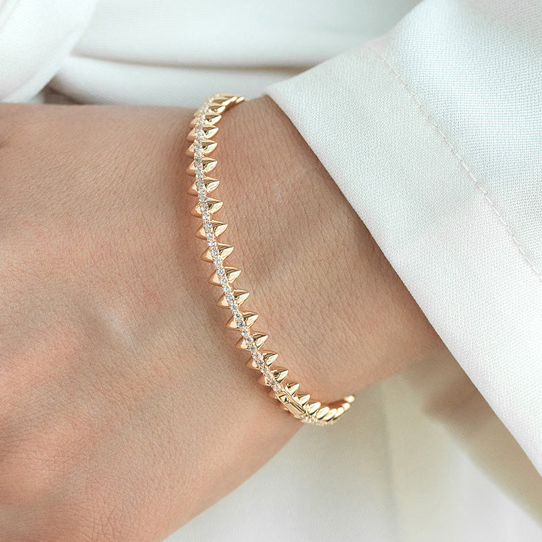 Gold bracelet with spike design on a wrist against a white background