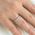 Close-up of a hand wearing a silver ring with small diamonds on a neutral background