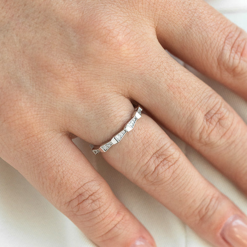 Close-up of a hand wearing a silver ring with small diamonds on a neutral background
