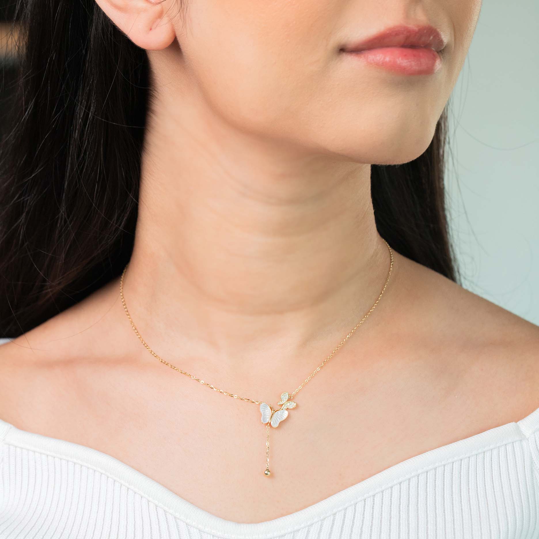 A person viewed from the side wearing a gold-toned necklace with a butterfly pendant.