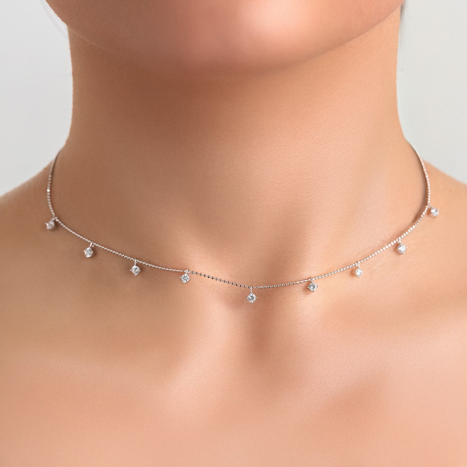 Delicate silver necklace with small pendants on a model against a neutral background