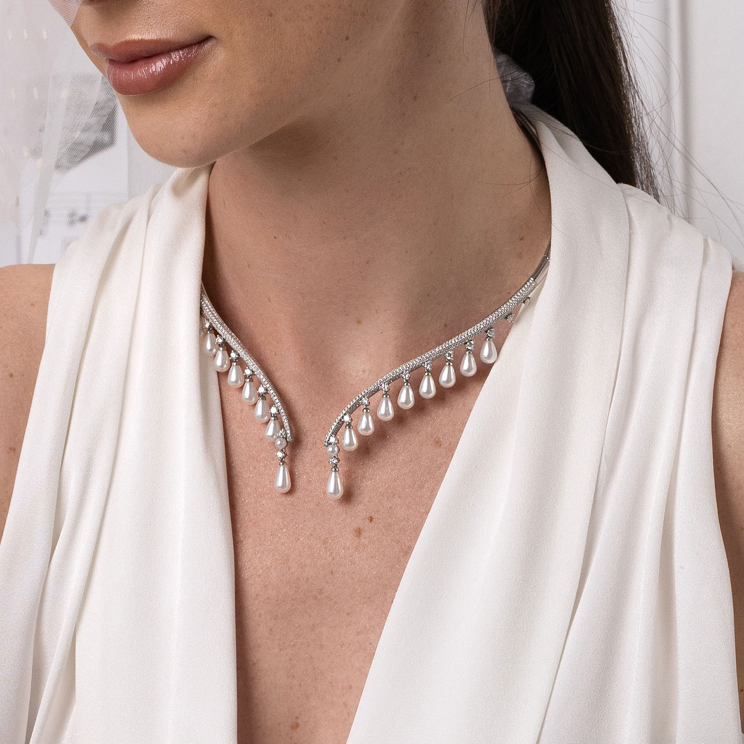 Close-up of a woman wearing a delicate silver necklace with teardrop pendants against a neutral background.