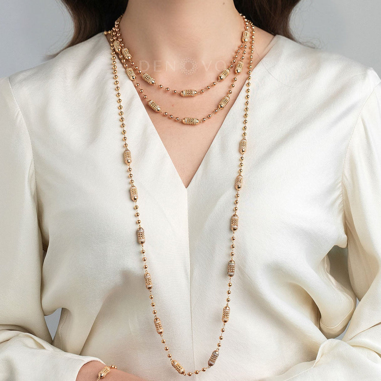 Woman wearing a long gold necklace with a plain background