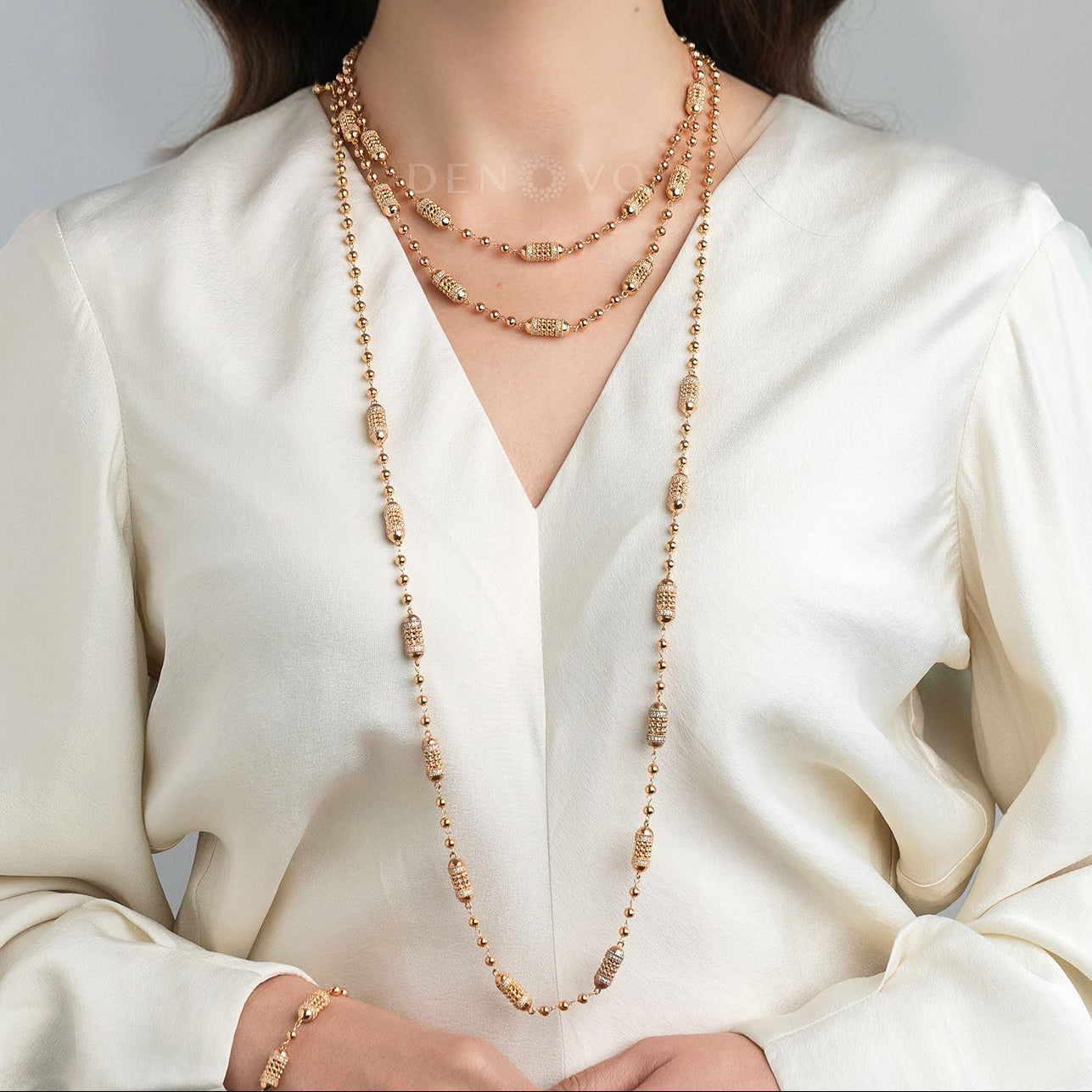 Woman wearing a long gold necklace with a plain background