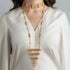 Gold necklace with fringe detail worn by a person in a white outfit