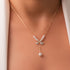 A gold-plated sterling silver necklace with a bow-shaped pendant featuring zircon stones and a faux pearl, displayed on a mannequin wearing a white coat.