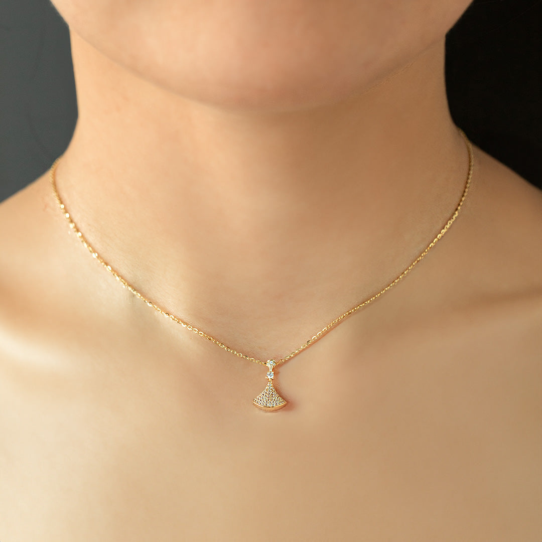 A person showing a short necklace with a gold-plated chain and a triangular pendant.