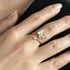 Gold butterfly ring on a person's finger against a neutral background