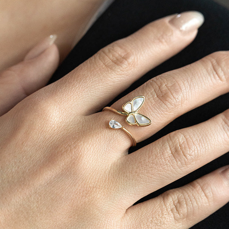 Gold butterfly ring on a person's finger against a neutral background