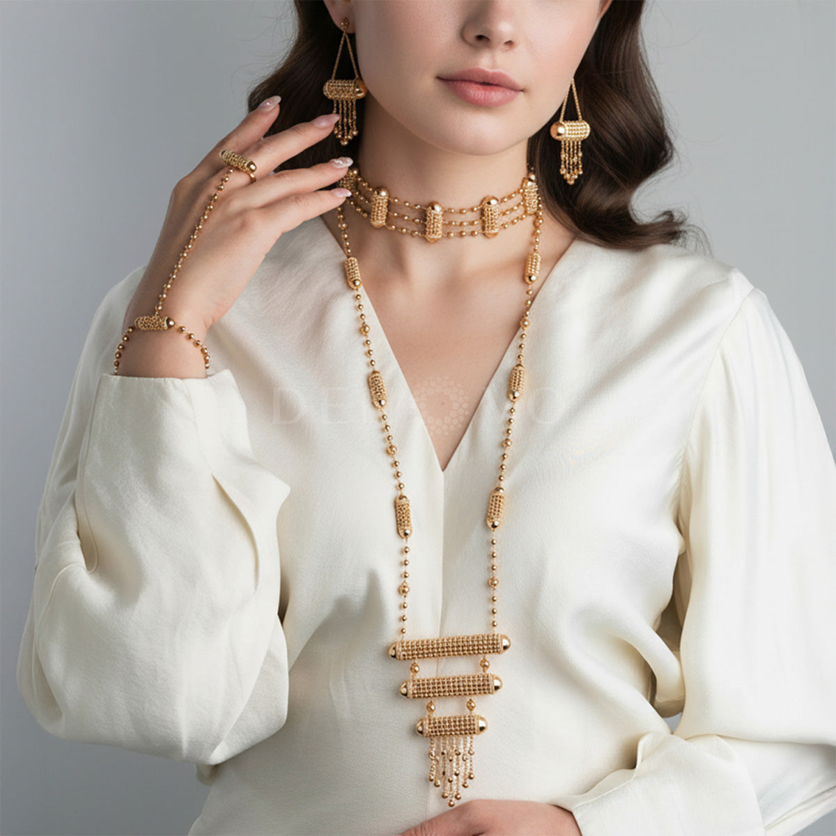 Woman wearing a gold necklace, bracelet, and earrings against a gray background