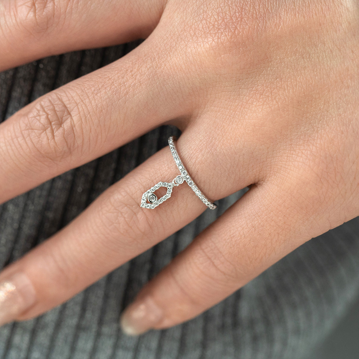 Silver ring with a small gemstone on a person's finger against a blurred background