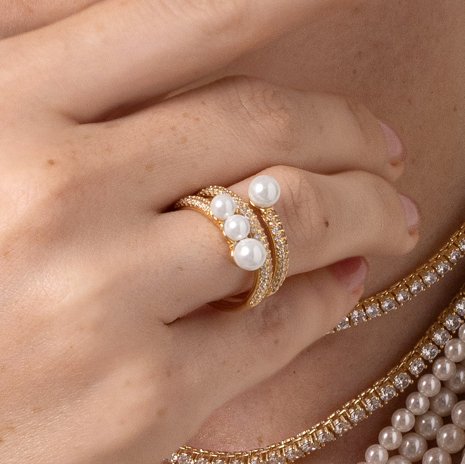 Gold ring with pearls on a hand against a black background