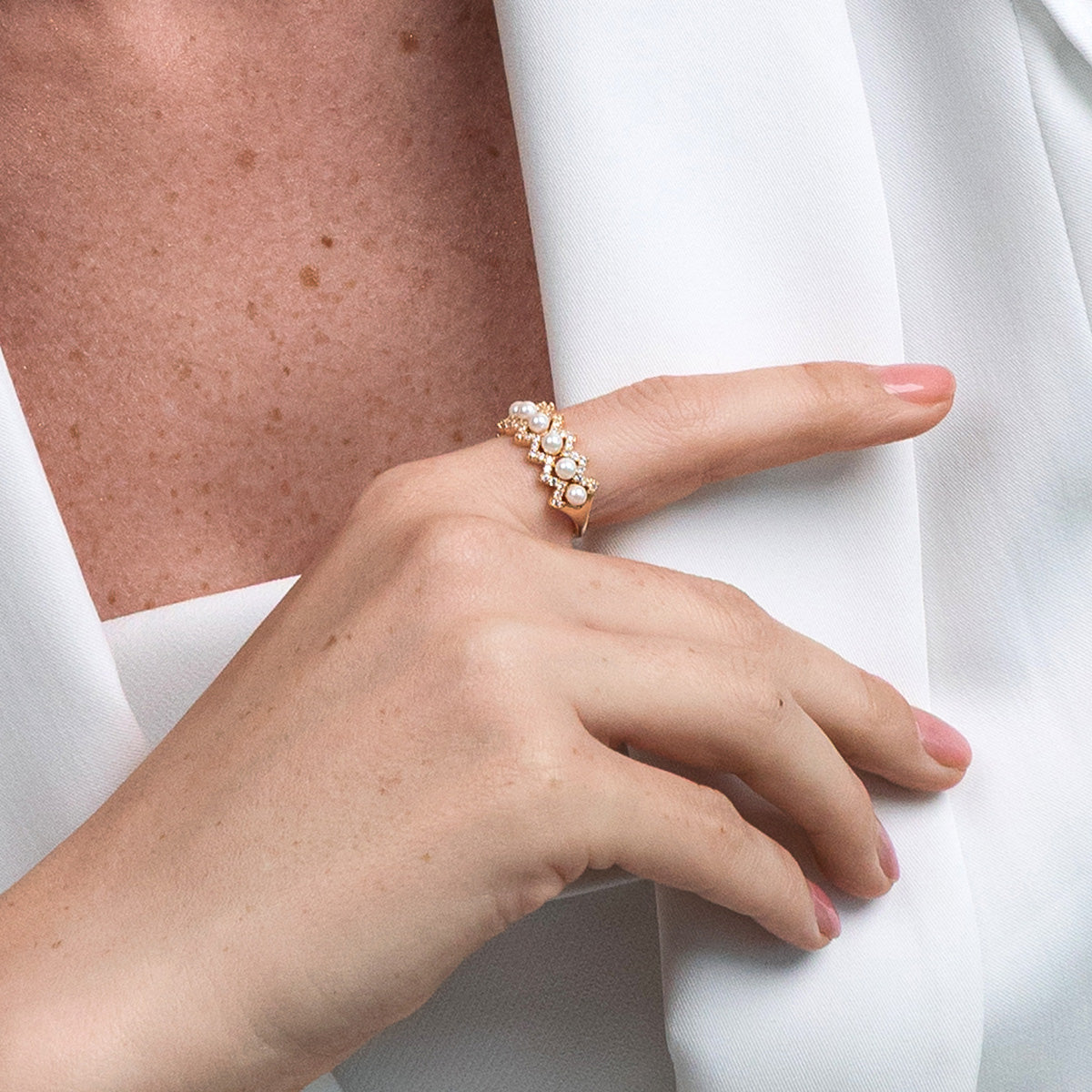 Hand wearing a gold ring with pearls on a white background