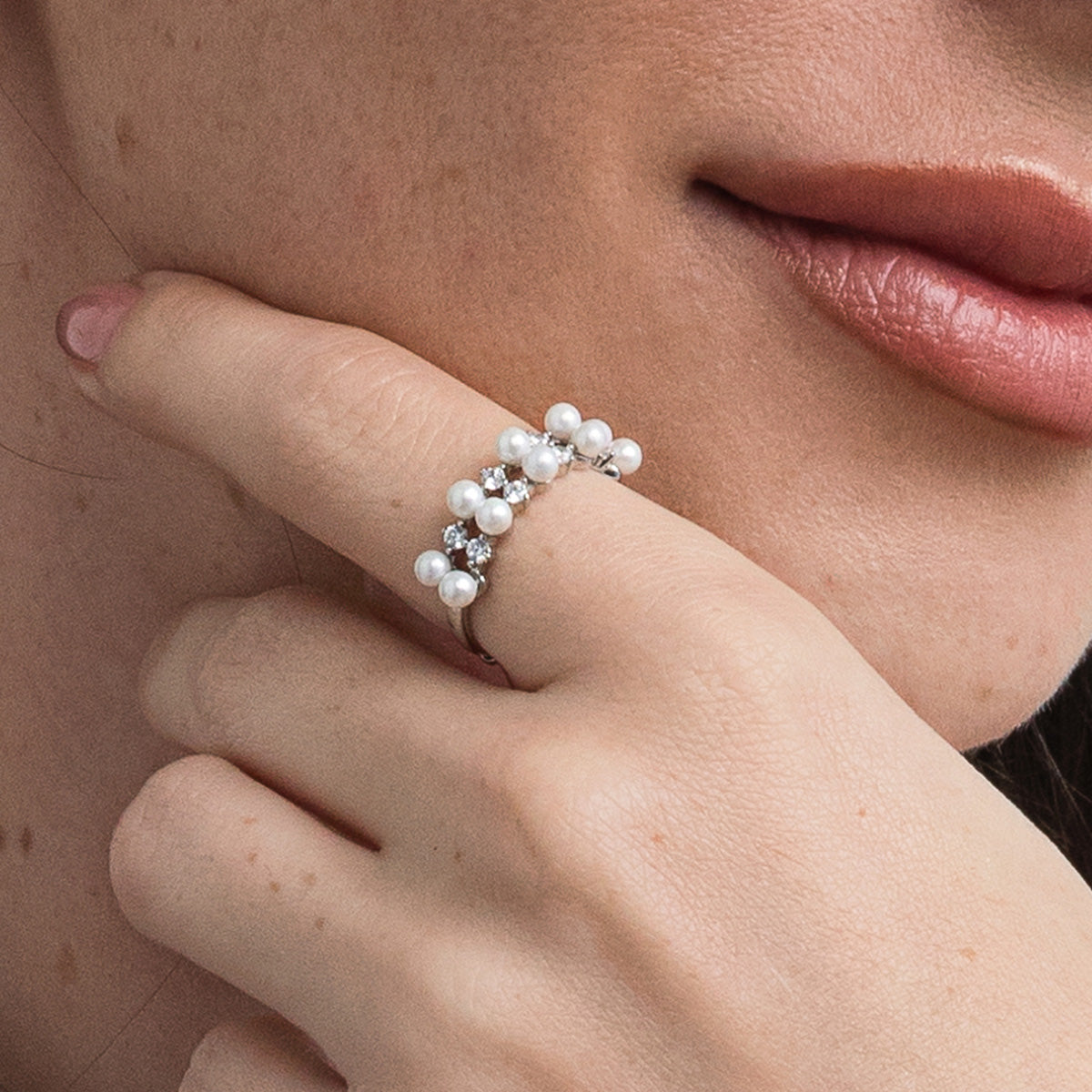 Close-up of a hand wearing a pearl ring with a blurred background