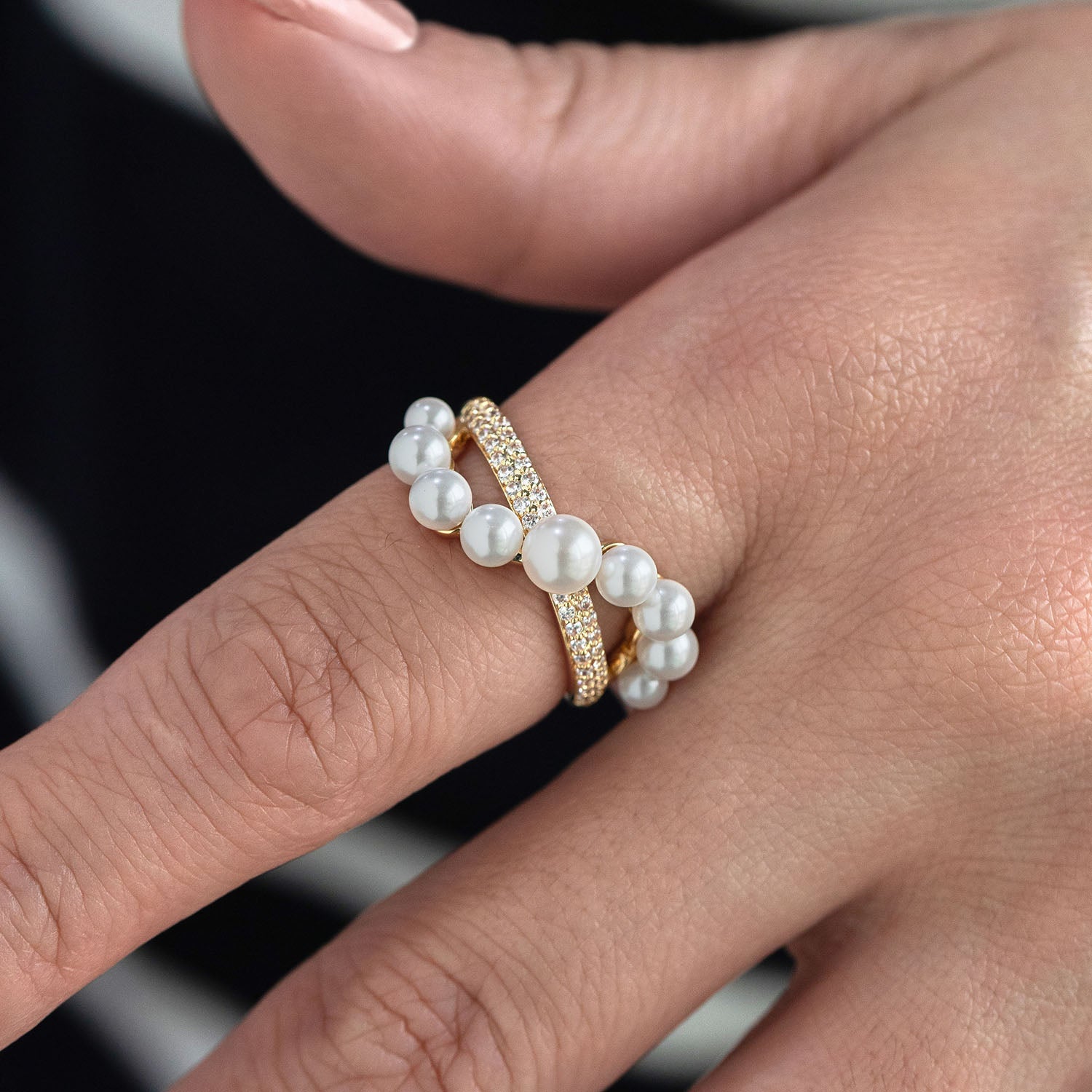 Gold ring with pearls on a finger against a blurred background