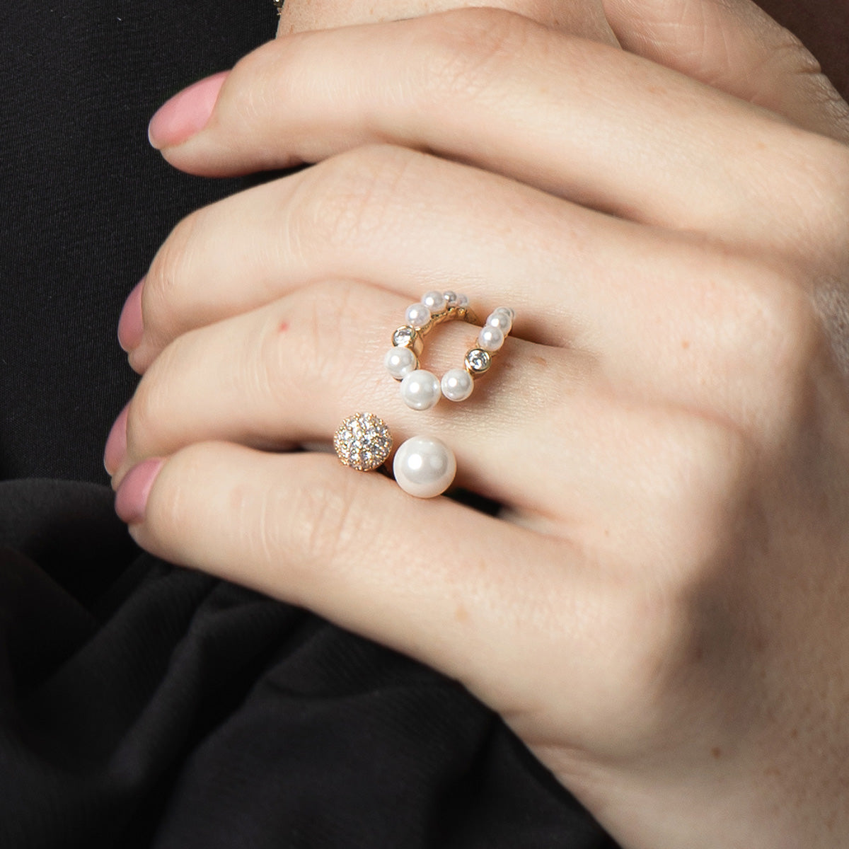 Close-up of a hand wearing two pearl rings on a black background