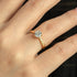 A gold-colored solitaire ring with a clear rounded stone on a person's finger.