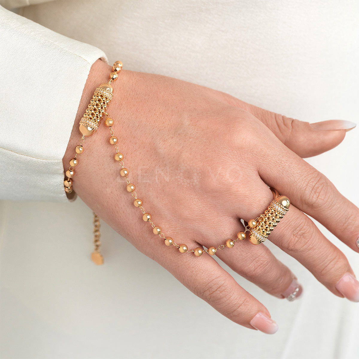 Hand wearing a gold bracelet and ring on a white background