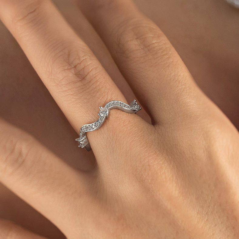 Silver ring with a wavy design on a person's finger against a neutral background