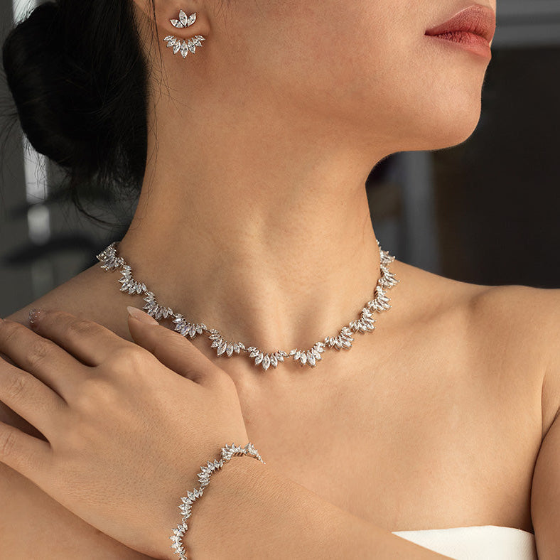 Close-up of a woman wearing a diamond necklace, earrings, and bracelet against a dark background.