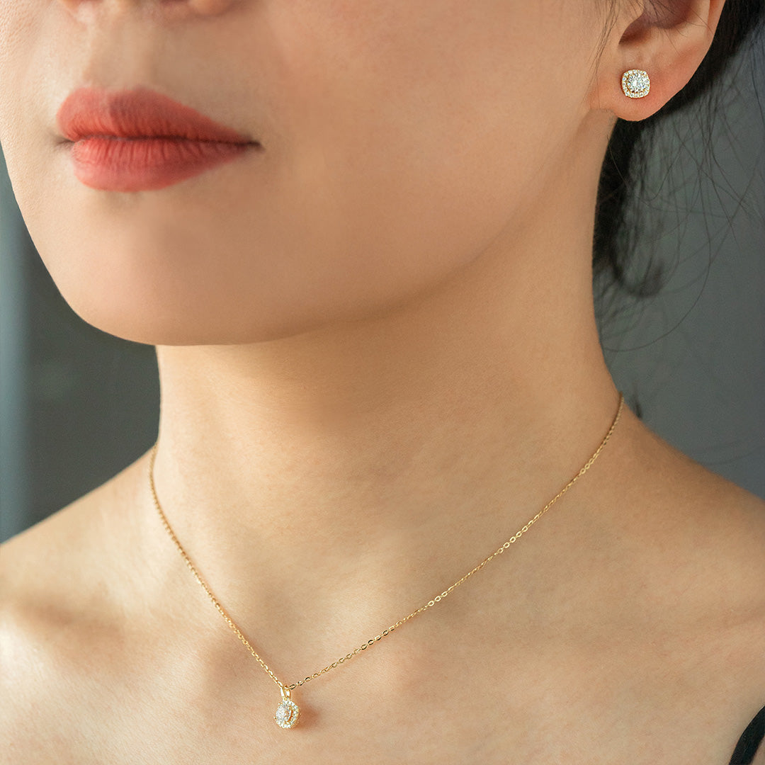 A close-up image of a woman wearing a gold-plated necklace and earrings set with a single diamond-like stone.
