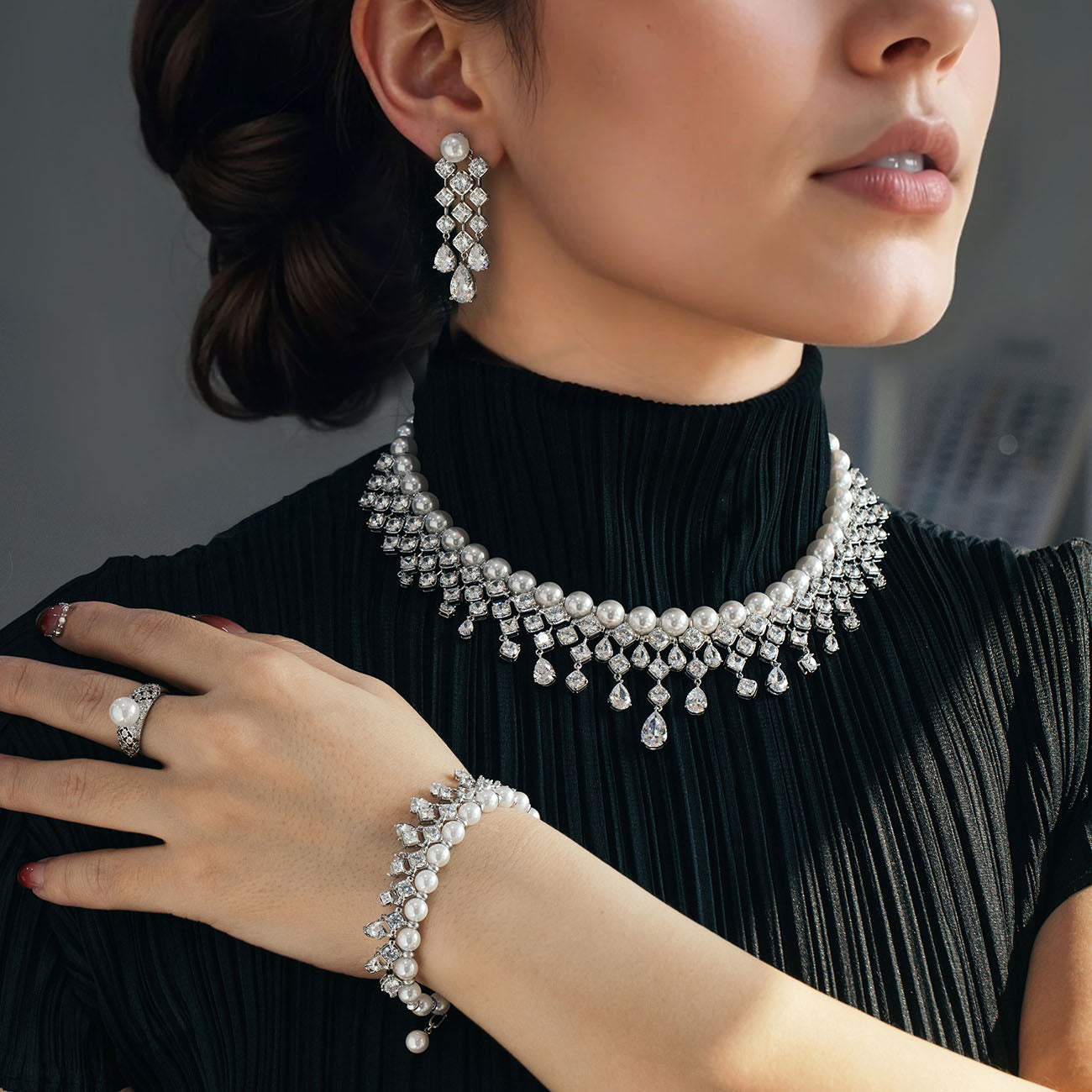 A person wearing a rhodium-plated necklace set with zircon stones, consisting of a long necklace and a pair of earrings.