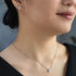 Close-up of a woman wearing a delicate necklace and earrings against a neutral background