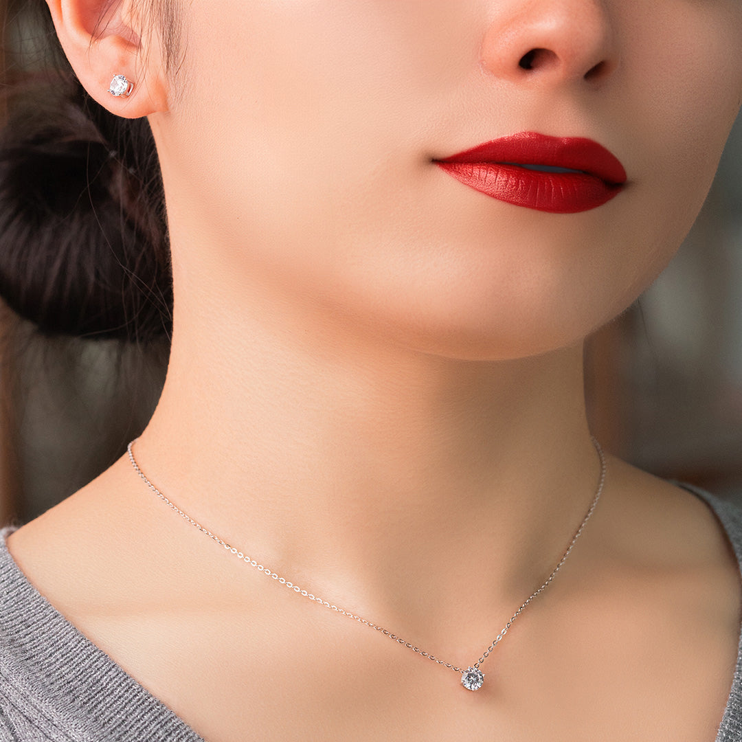 A person wearing a red lipstick and a gold-colored necklace with a solitaire design, paired with matching earrings.