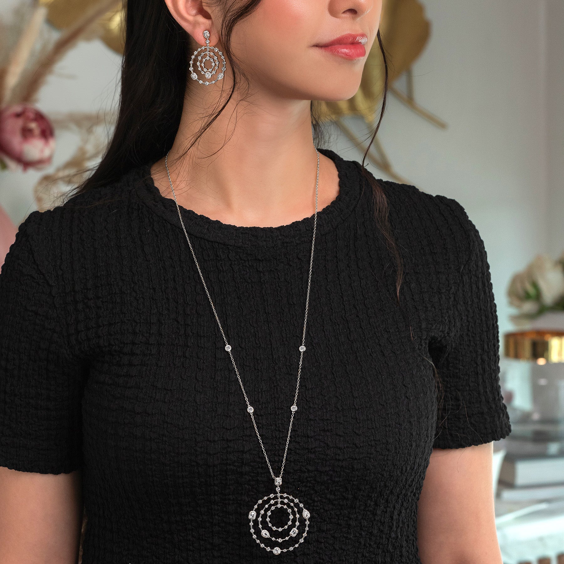 Woman wearing a black top with a long silver necklace and earrings.